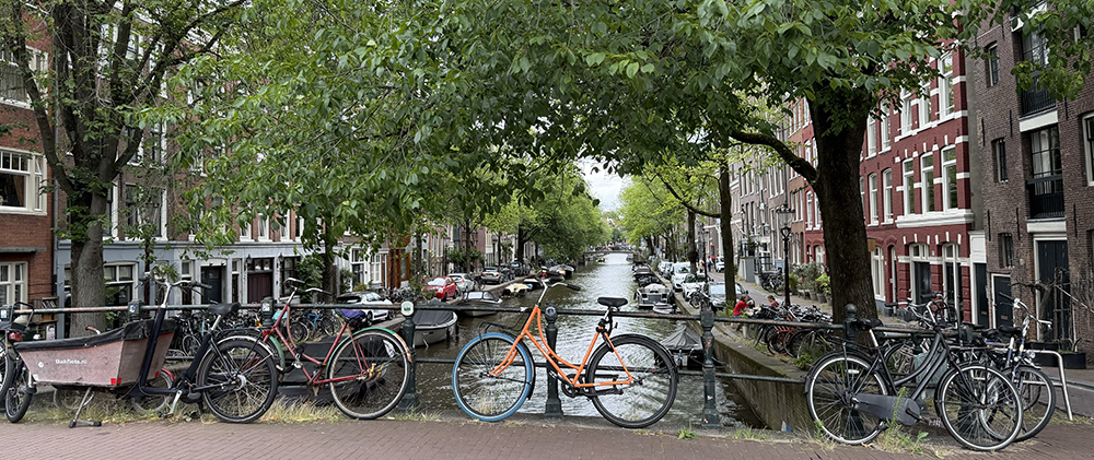 View from a foot bridge of a canal in Amsterdam with canopy trees on both sides and an orange bicycle in front and center.